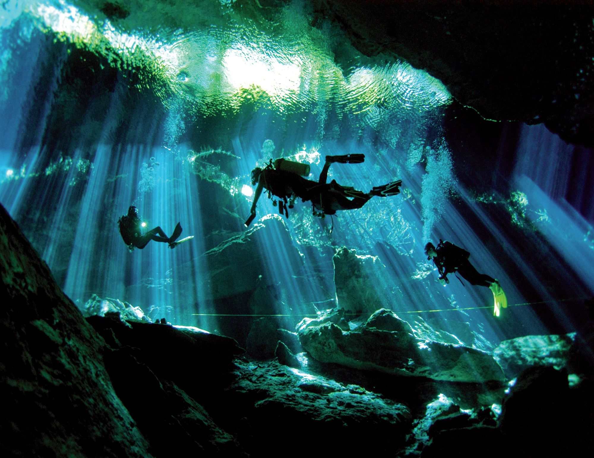Divers under sunbeams in a Riviera Maya cenote